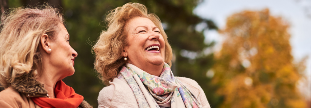 2 Elderly women sitting on a park bench with an autumnal background