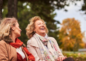 2 Elderly women sitting on a park bench with an autumnal background