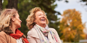 2 Elderly women sitting on a park bench with an autumnal background