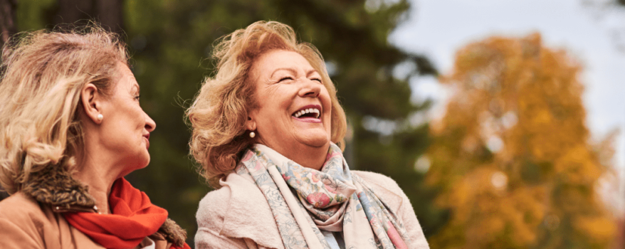 2 Elderly women sitting on a park bench with an autumnal background